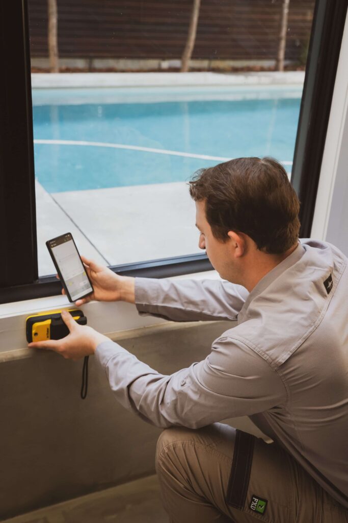 Ben using a yellow Termatrac iTraker Pro against a wall beside a window